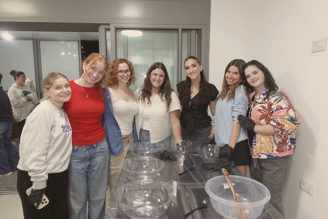 Seven friends smiling around a table of mixing bowls at a challah bake